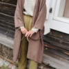 Front of an unfastened long heavy cacao linen jacket paired with a linen top and trousers