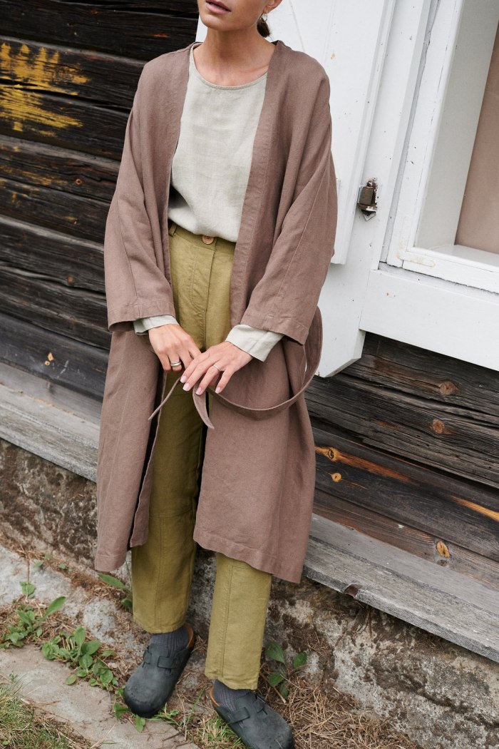 Front of an unfastened long heavy cacao linen jacket paired with a linen top and trousers