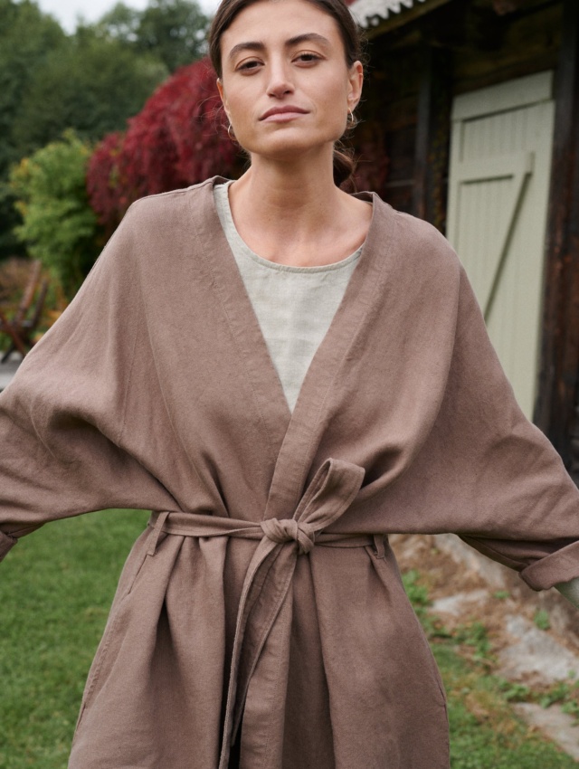 A model in a heavy cacao linen jacket with loose sleeves and a fastened matching belt