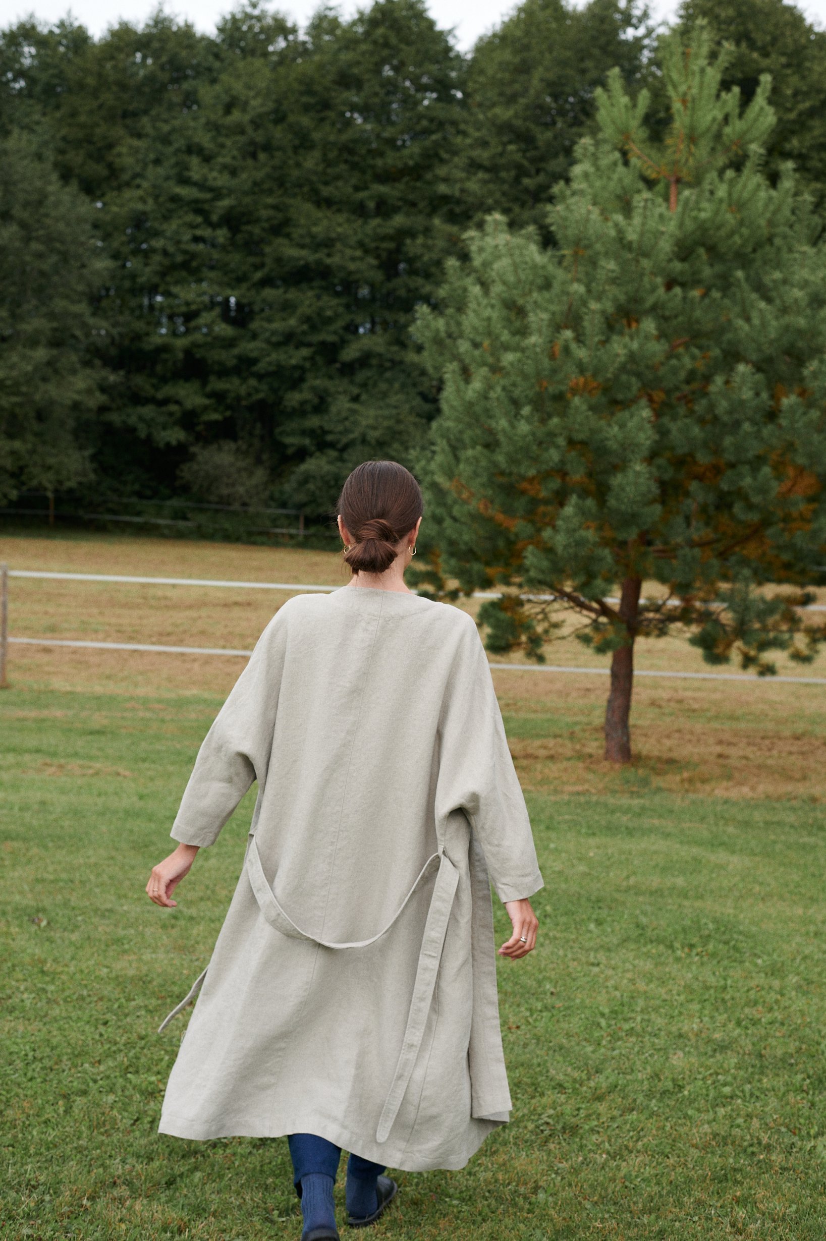 Model walking in nature wearing a long natural grey linen jacket