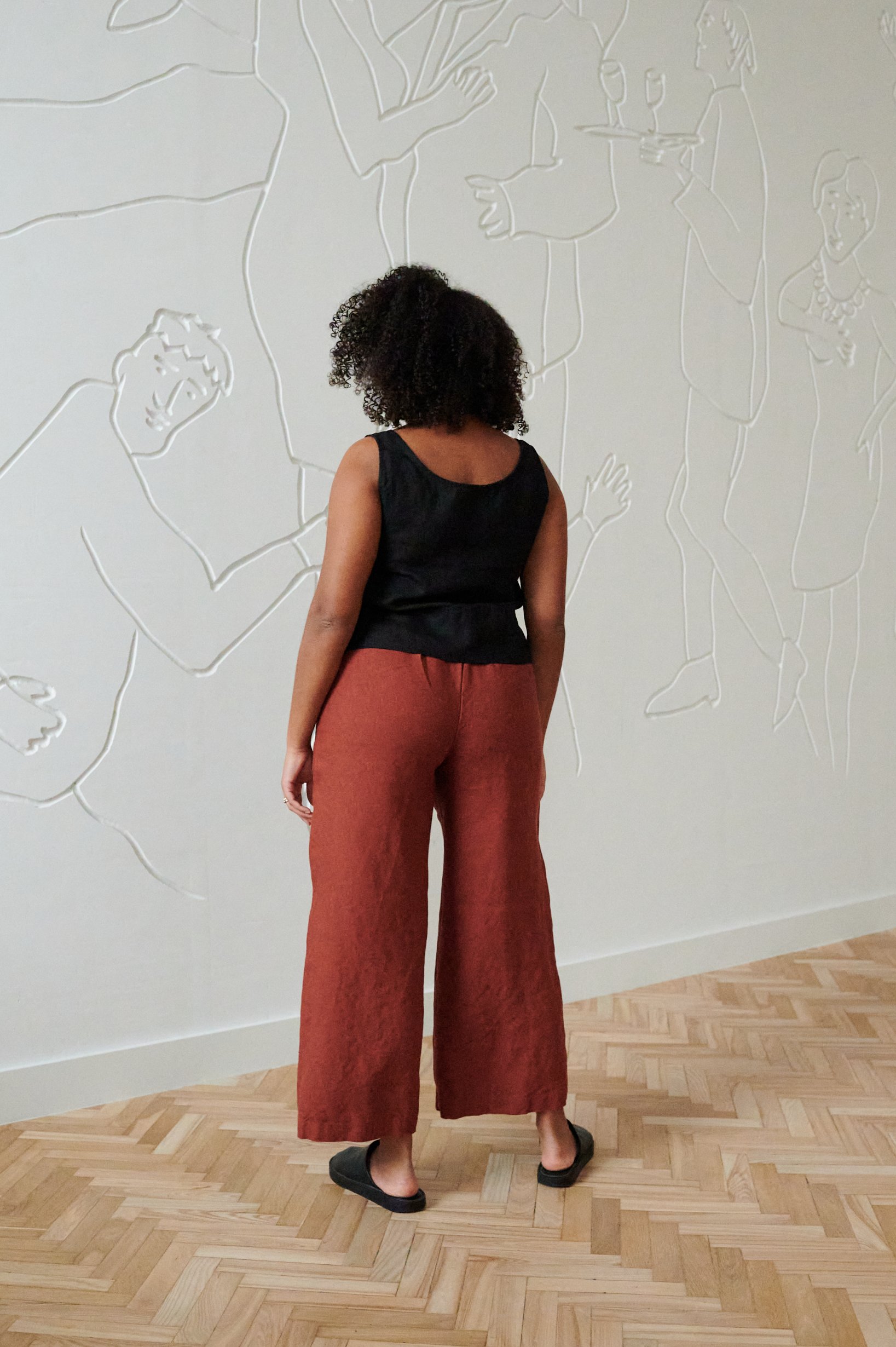 Back of a model in slightly cropped heavy linen trousers and a sleeveless linen top