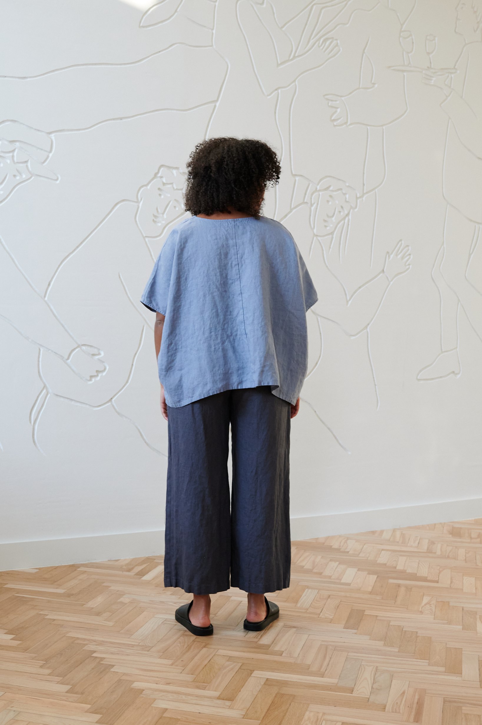 Back of a model wearing an oversized sky blue linen top and loose-fitting linen trousers