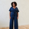 Front of a model in a navy blue linen jumpsuit with an attached belt fastened around the waist
