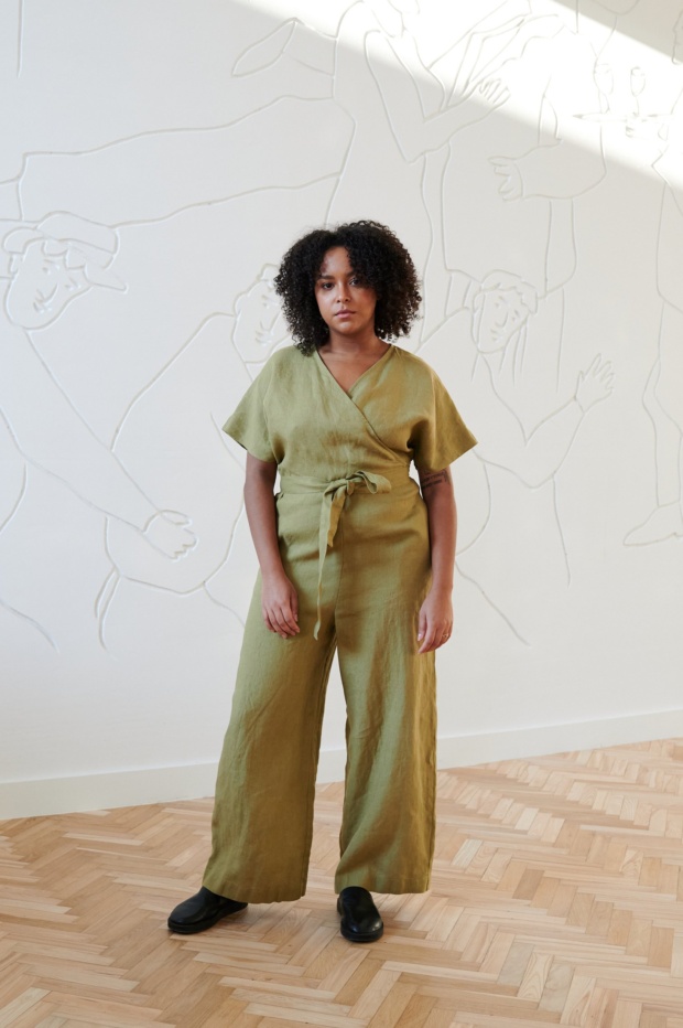 Front of a model wearing an olive linen jumpsuit with dropped shoulders and a plunging V-neck