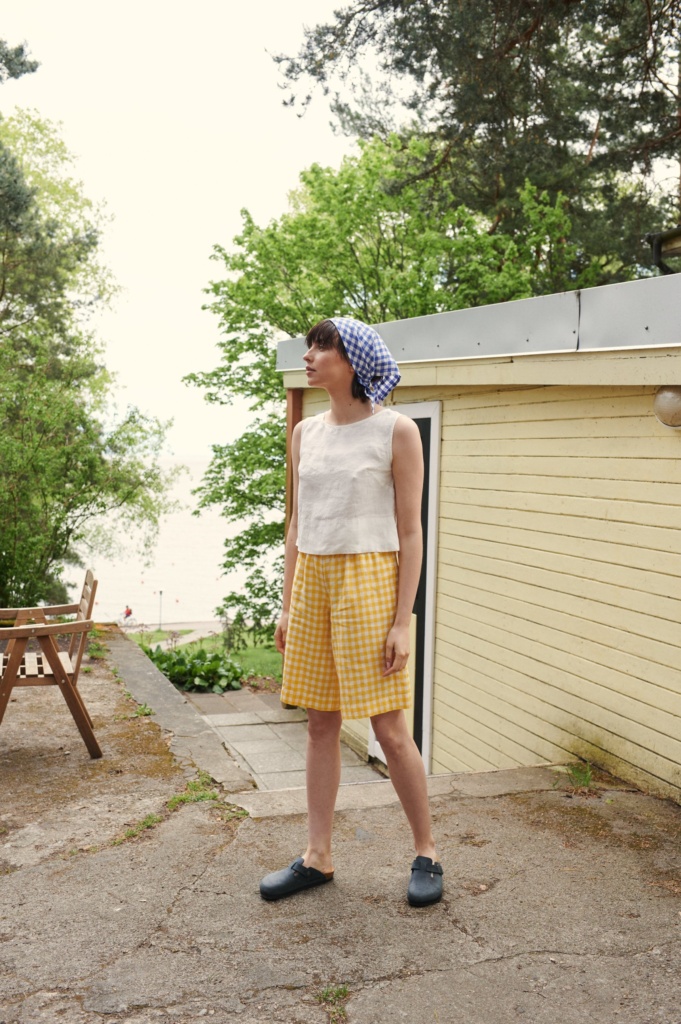 Model in yellow gingham linen shorts and a sleeves white linen top