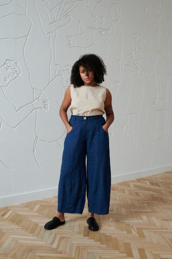 A woman wearing blue high waisted linen trousers and a beige dropped linen top