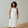Model in a long flared sleeveless linen dress with a straight across neckline