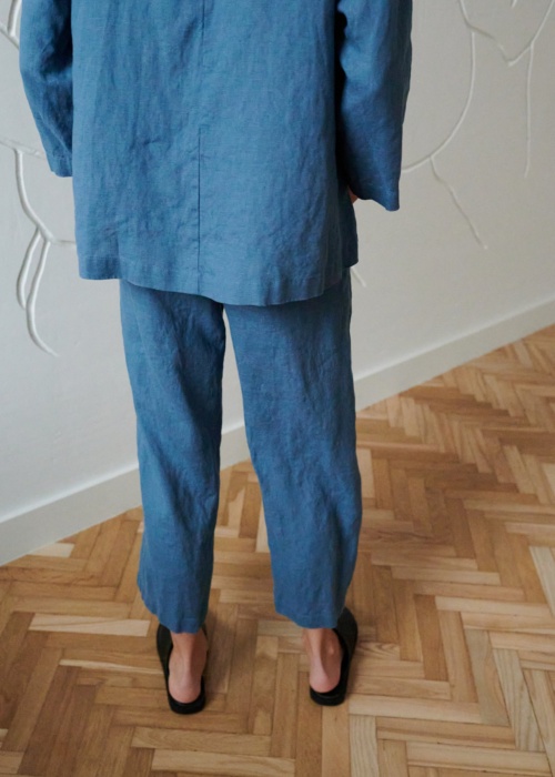 Back of a model in loose-fitting linen trousers and an oversized linen tunic