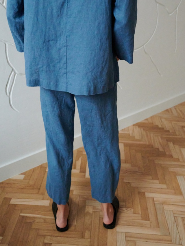 Back of a model in loose-fitting linen trousers and an oversized linen tunic