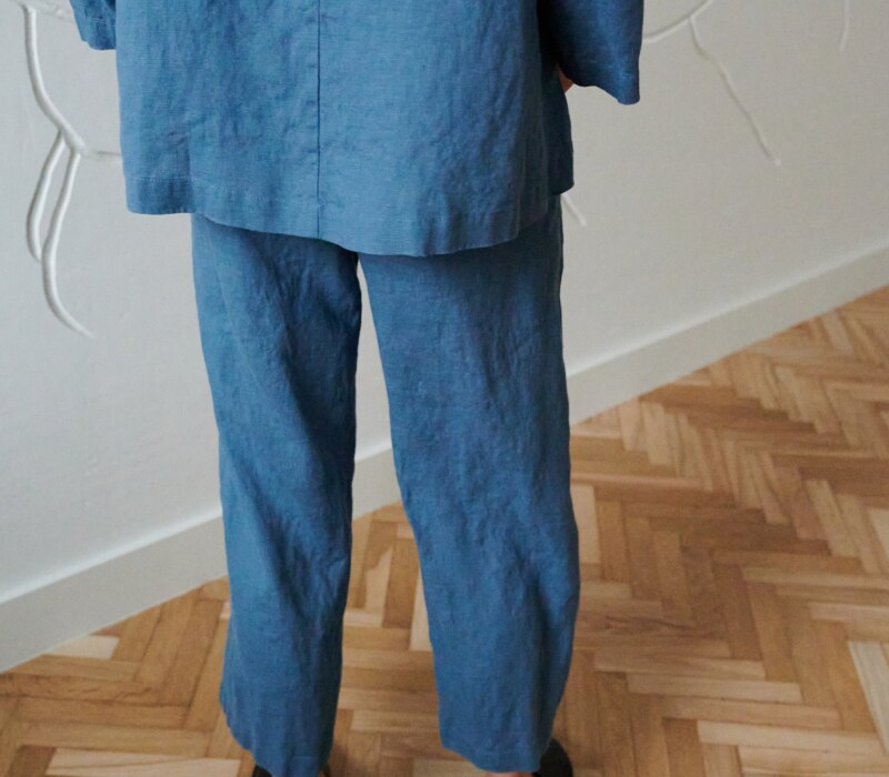 Back of a model in loose-fitting linen trousers and an oversized linen tunic