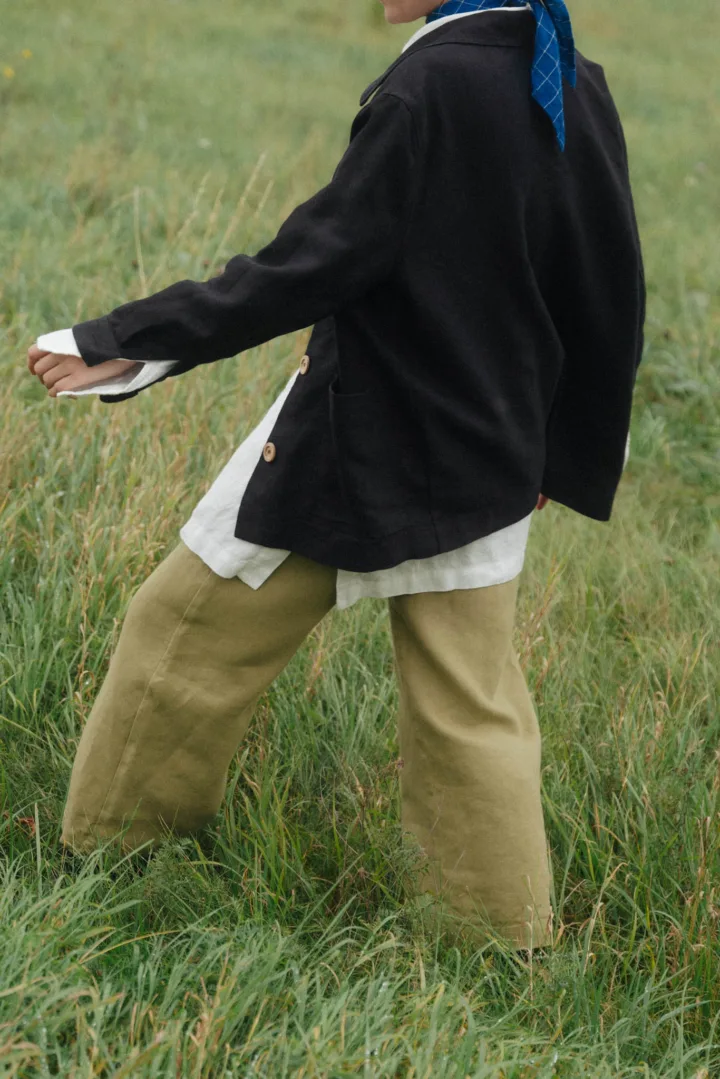 Olive green heavy linen trousers with a relaxed wide-leg cut, paired with a black jacket, white linen shirt and blue scarf