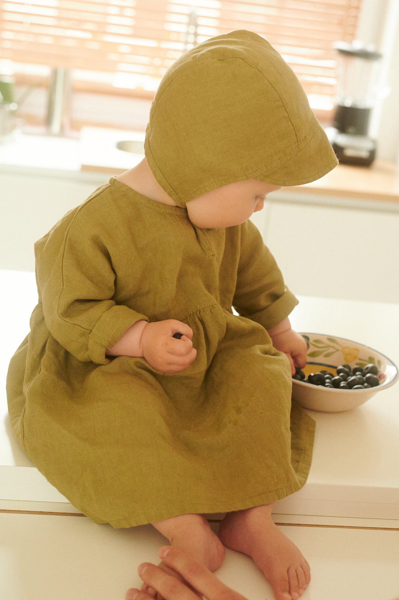 baby girl wearing linen bonnet and linen dress in olive color