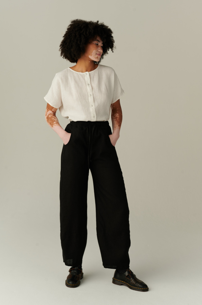 Girl wearing black barrel leg linen trousers and a white short sleeve linen shirt with snap buttons