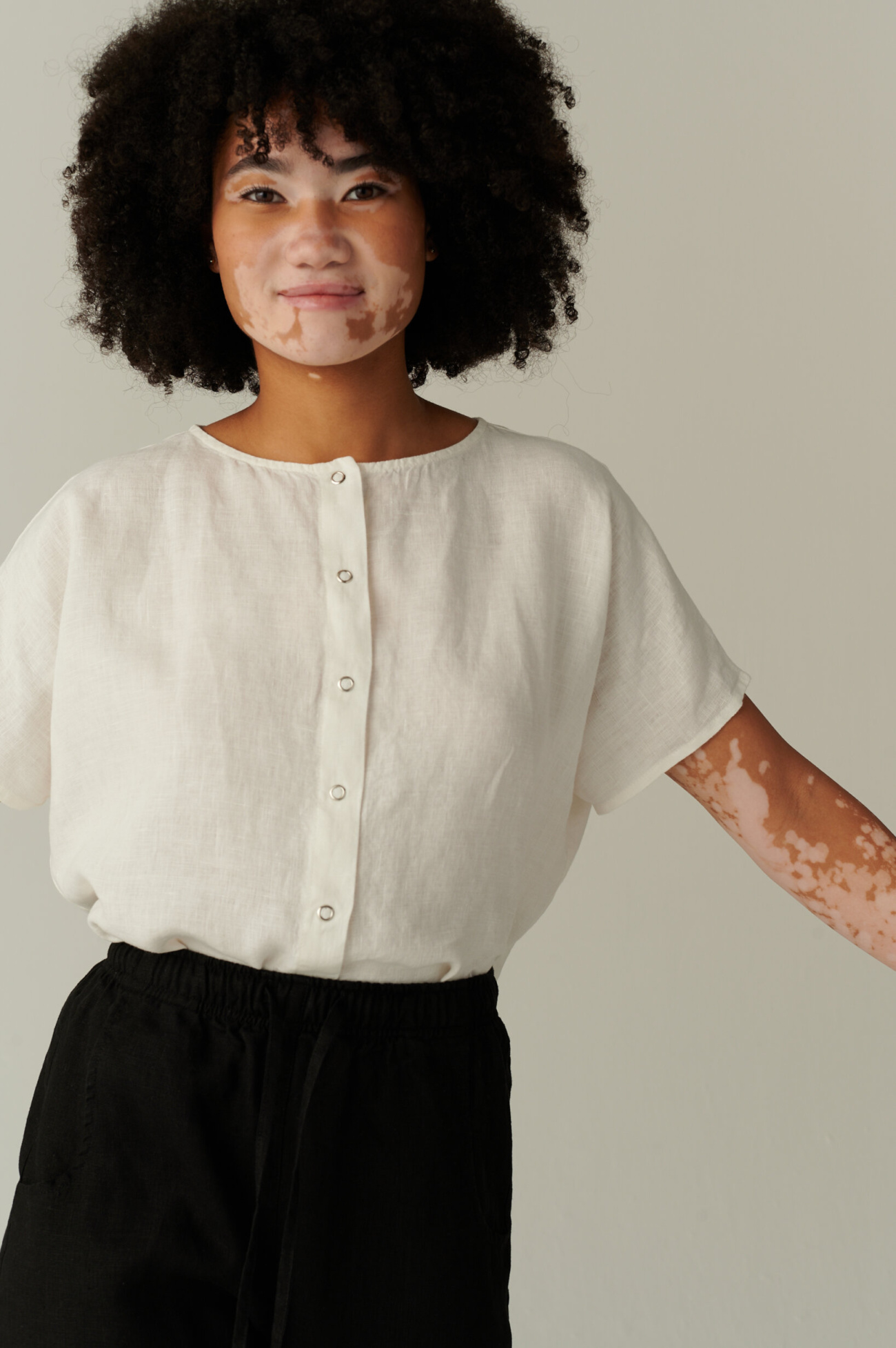 Relaxed fit white linen top with dropped shoulders and snap buttons tucked into black linen trousers