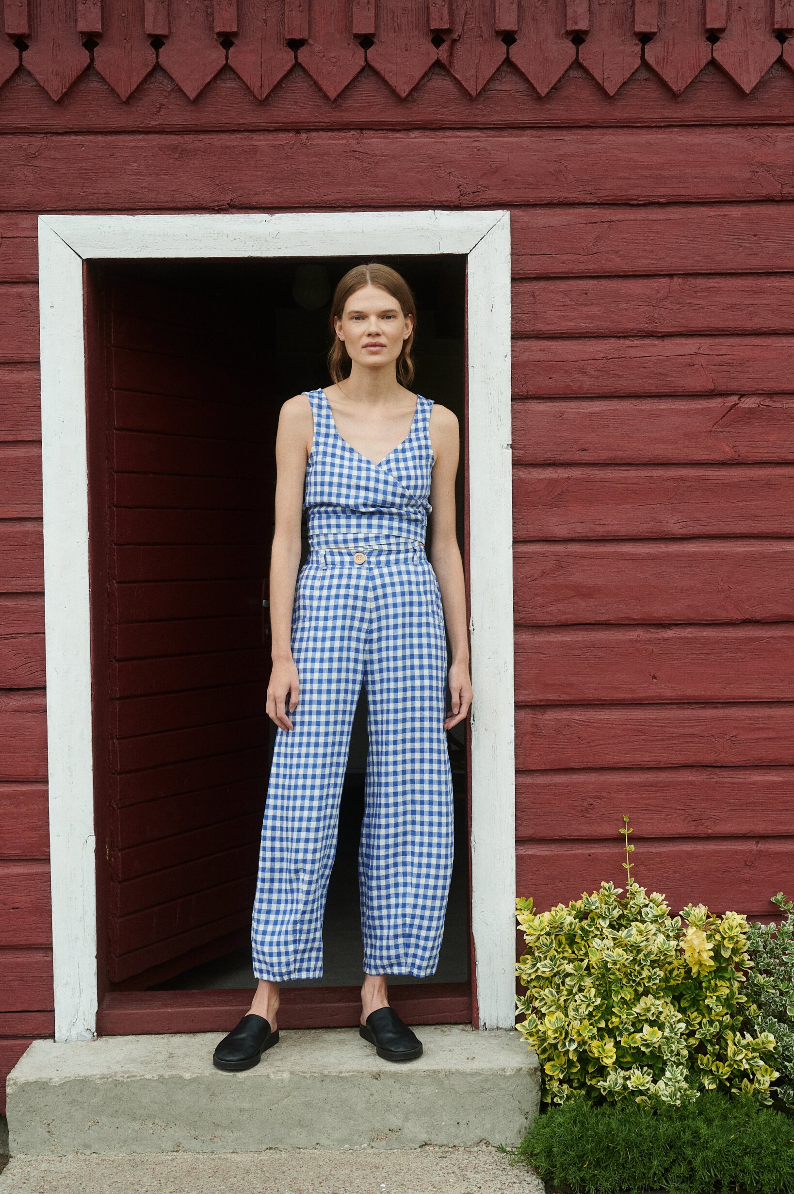 model standing wearing blue gingham linen set for summer of relaxed barrel leg trousers and V-neck wrap top