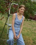 model in a garden wearing a set for summer - wrap top and relaxed trousers in blue gingham linen fabric