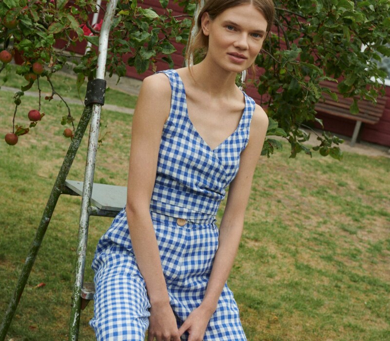 model in a garden wearing a set for summer - wrap top and relaxed trousers in blue gingham linen fabric