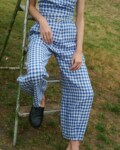 model sitting outside wearing blue gingham linen set of relaxed trousers and V-neck summer wrap top