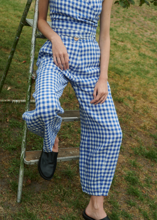 model sitting outside wearing blue gingham linen set of relaxed trousers and V-neck summer wrap top