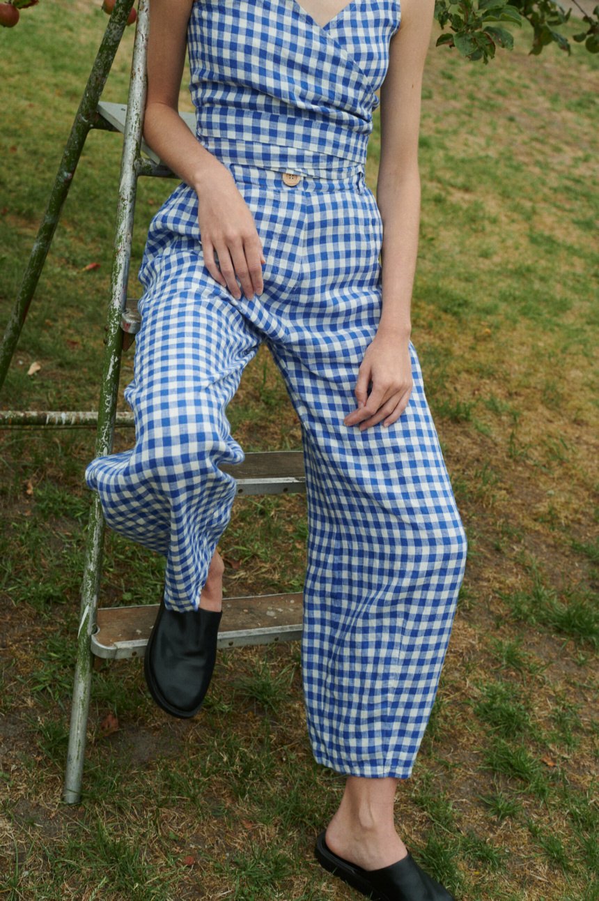 model sitting outside wearing blue gingham linen set of relaxed trousers and V-neck summer wrap top