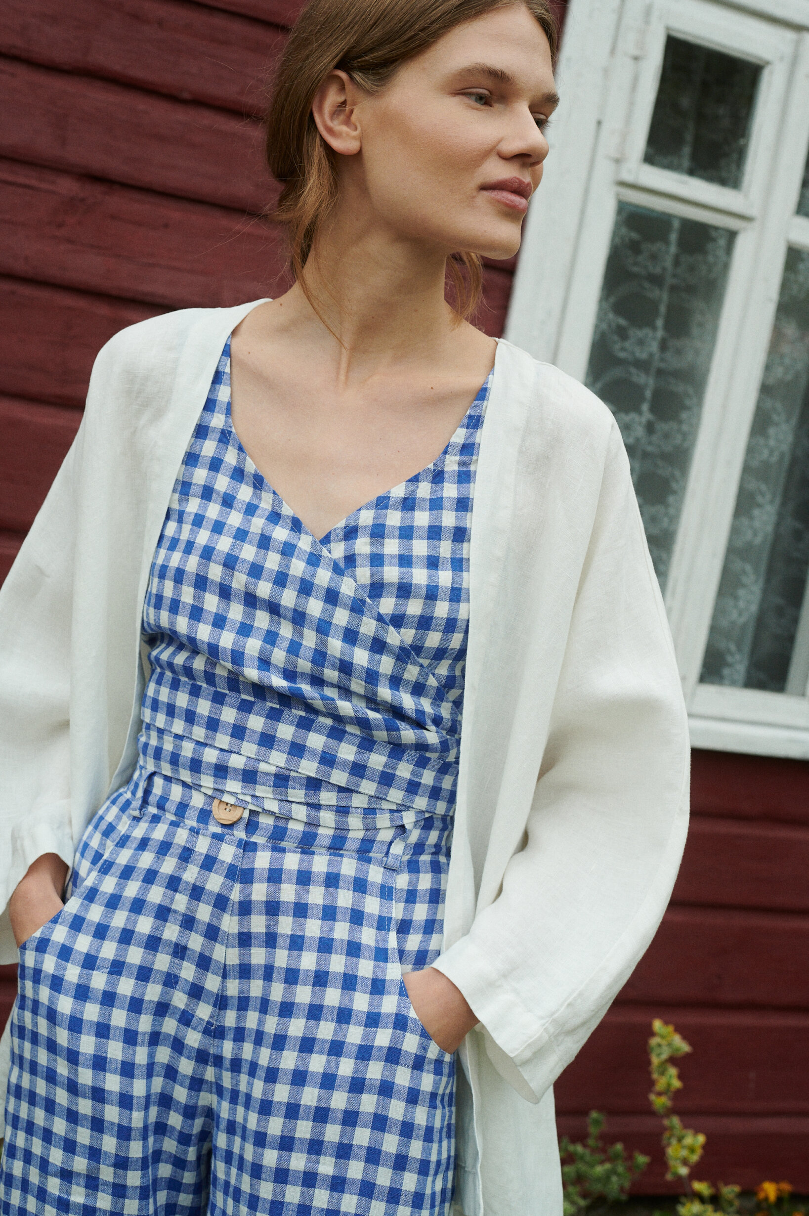 model wearing blue gingham summer linen set of relaxed trousers and wrap top with an oversized linen jacket in milky white