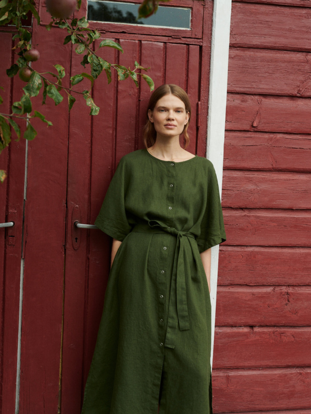 model wearing oversized summer linen dress in forest green with snap openings in a garden