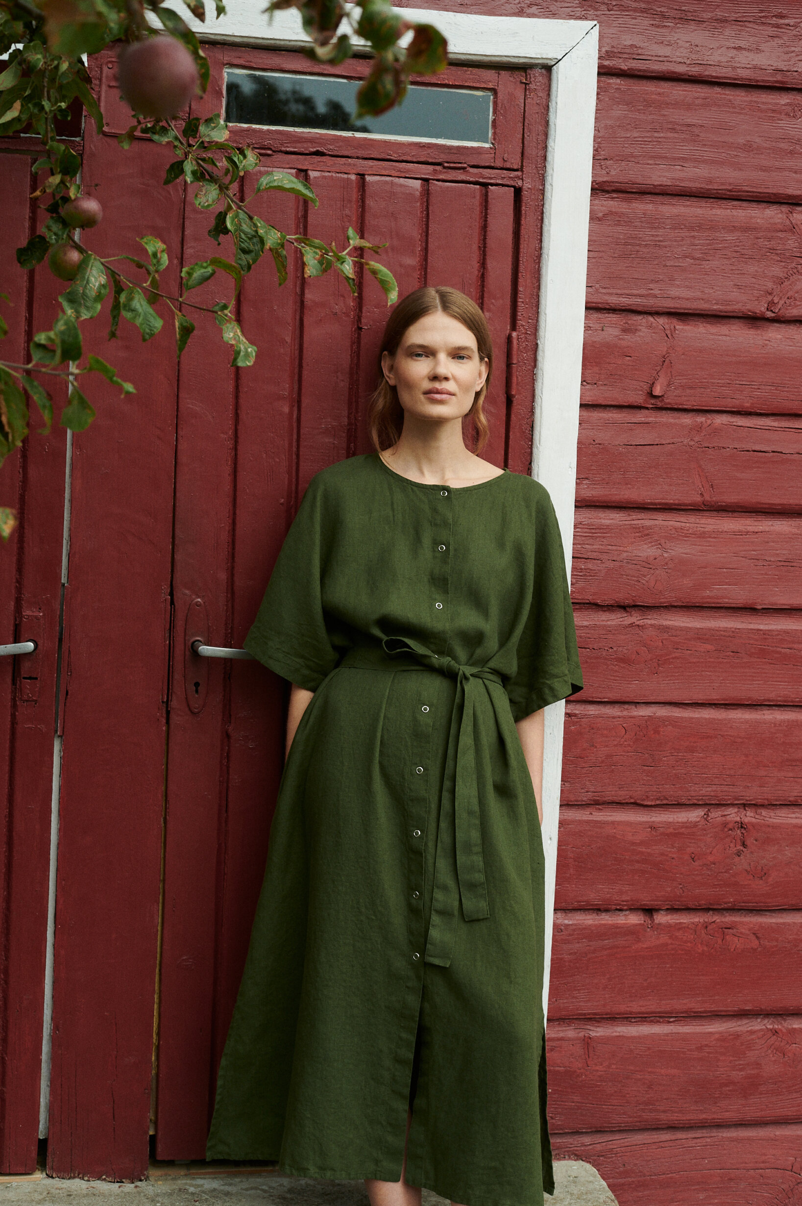 model wearing oversized summer linen dress in forest green with snap openings in a garden