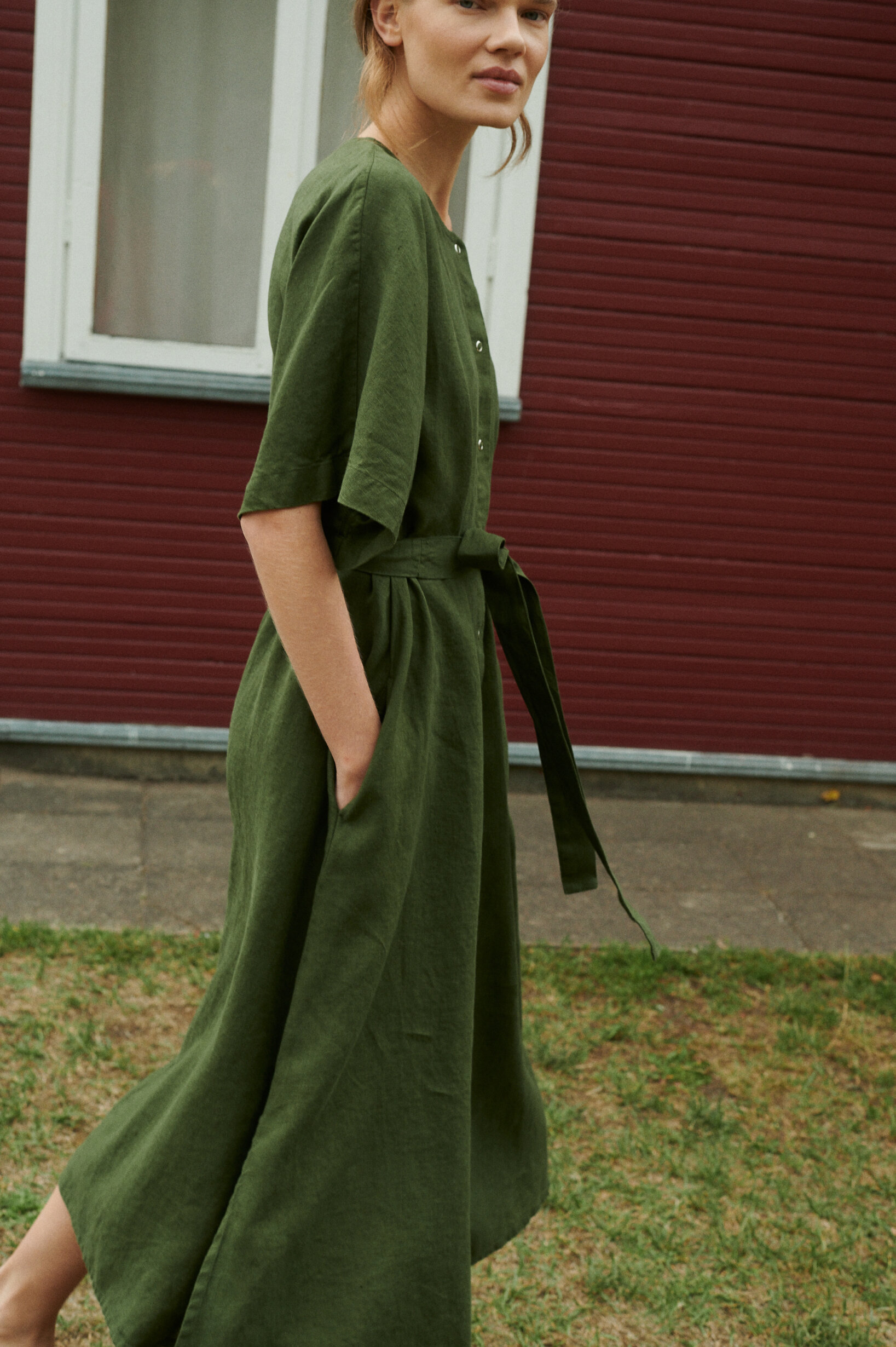 model wearing oversized summer linen dress in forest green with snap openings and pockets outside the summer house