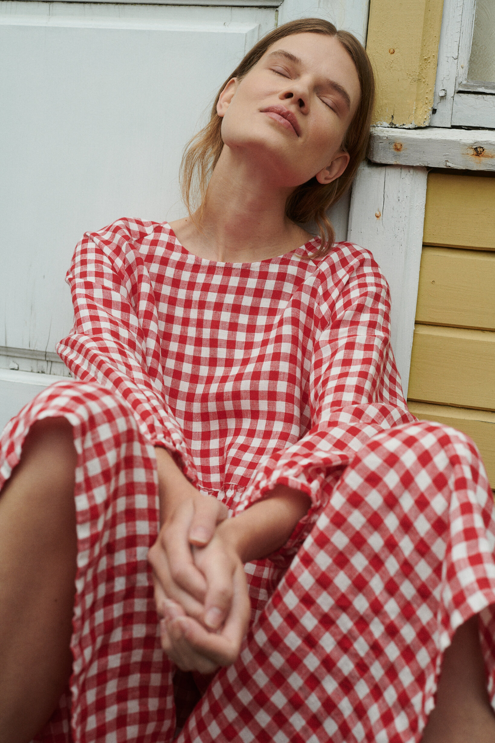 a close up shot of model wearing oversized red gingham linen dress outside