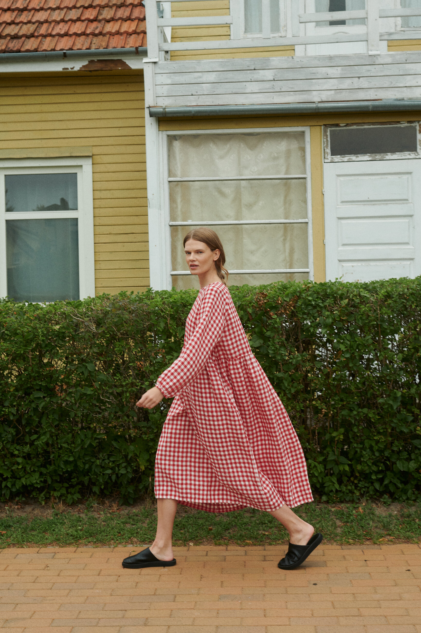 model walking and posing wearing oversized red gingham linen dress near the summer house