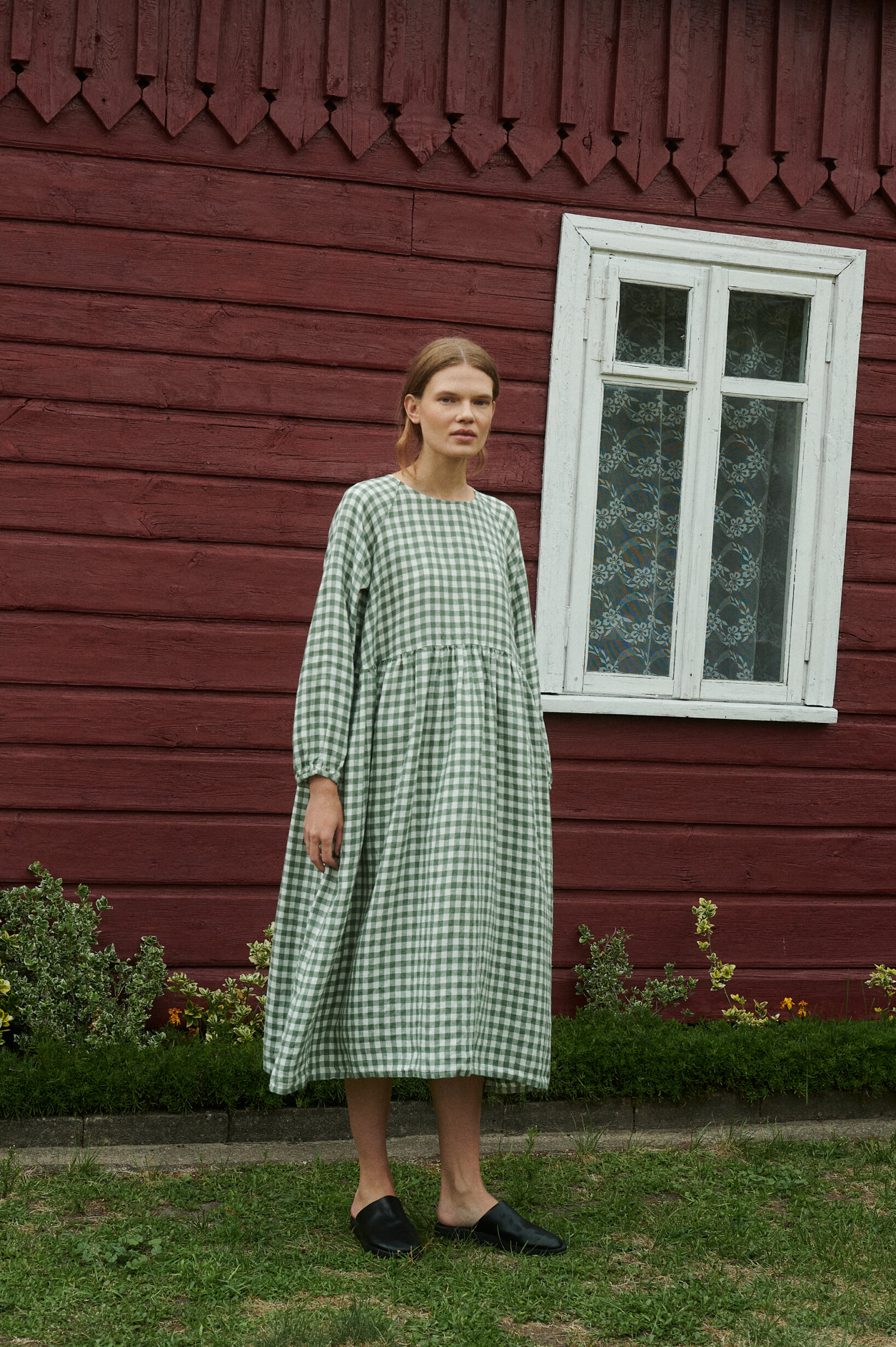 model in a summer garden posing with an oversized green gingham linen dress with full length sleeves and pockets