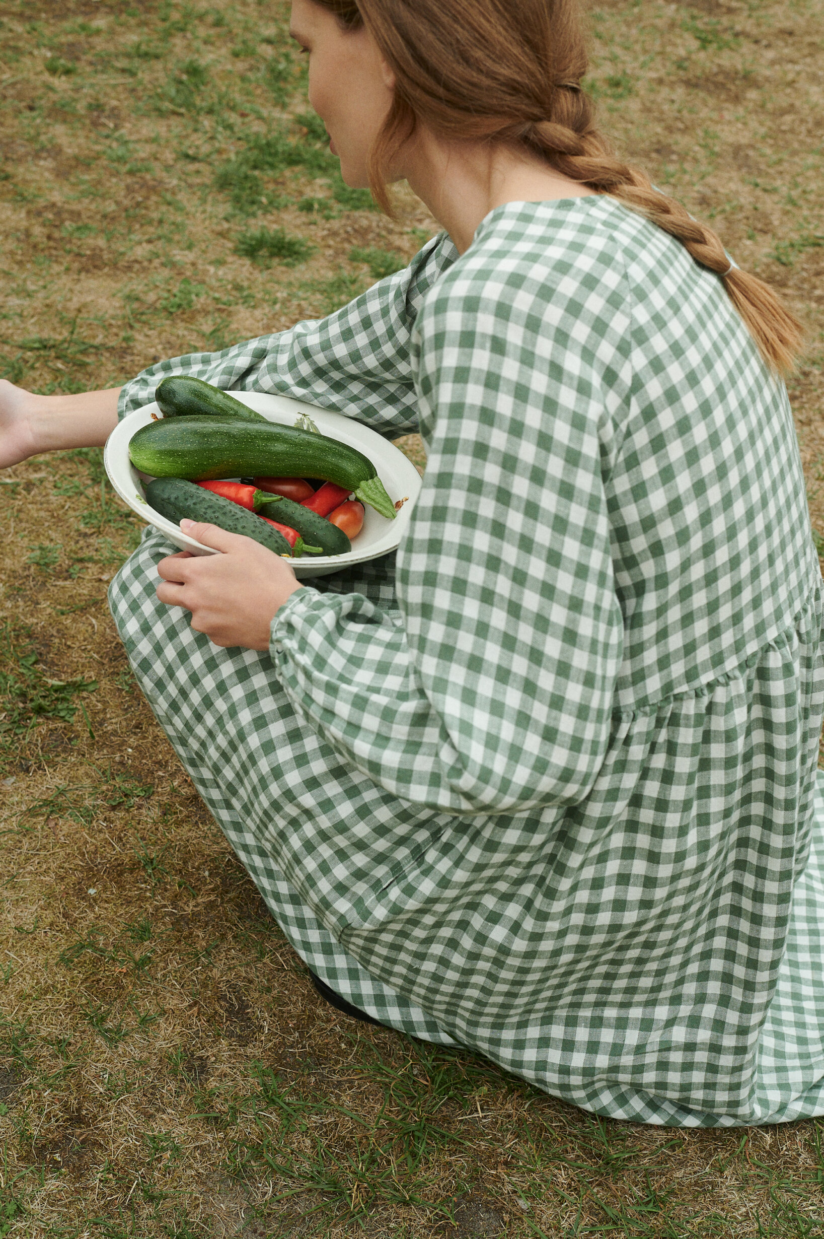 a close up of woman weaing oversized green gingham linen dress with full length sleeves and holding a plate of vegetables