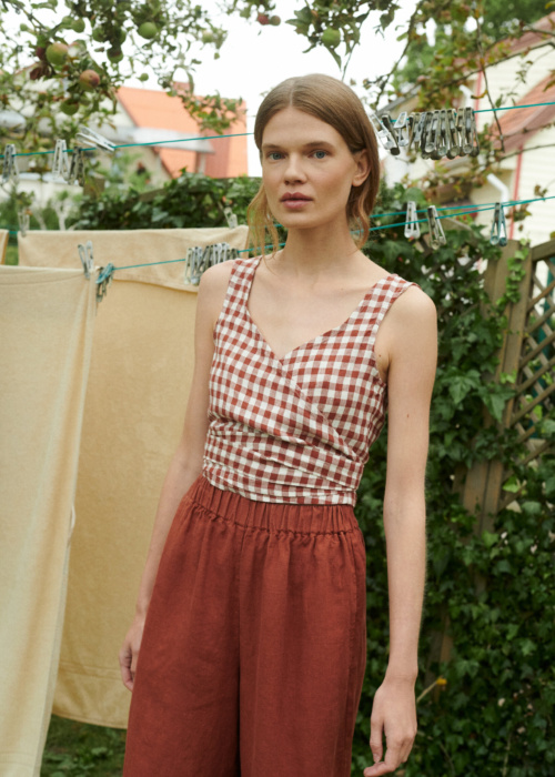 model in a garden wearing gingham linen summer top in V-neck and wide leg linen trousers