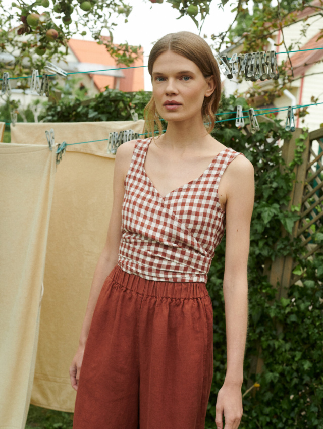 model in a garden wearing gingham linen summer top in V-neck and wide leg linen trousers