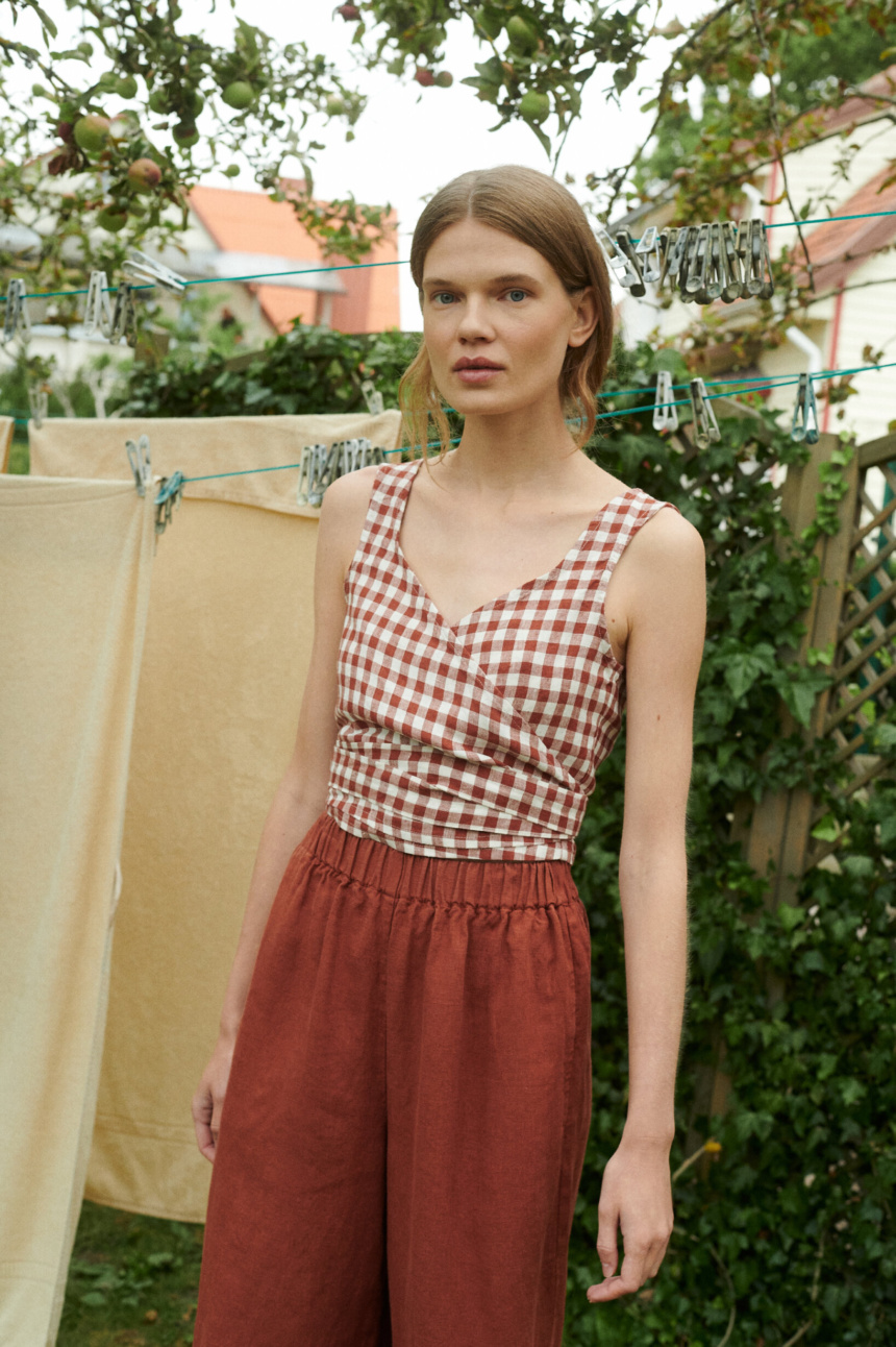 model in a garden wearing gingham linen summer top in V-neck and wide leg linen trousers