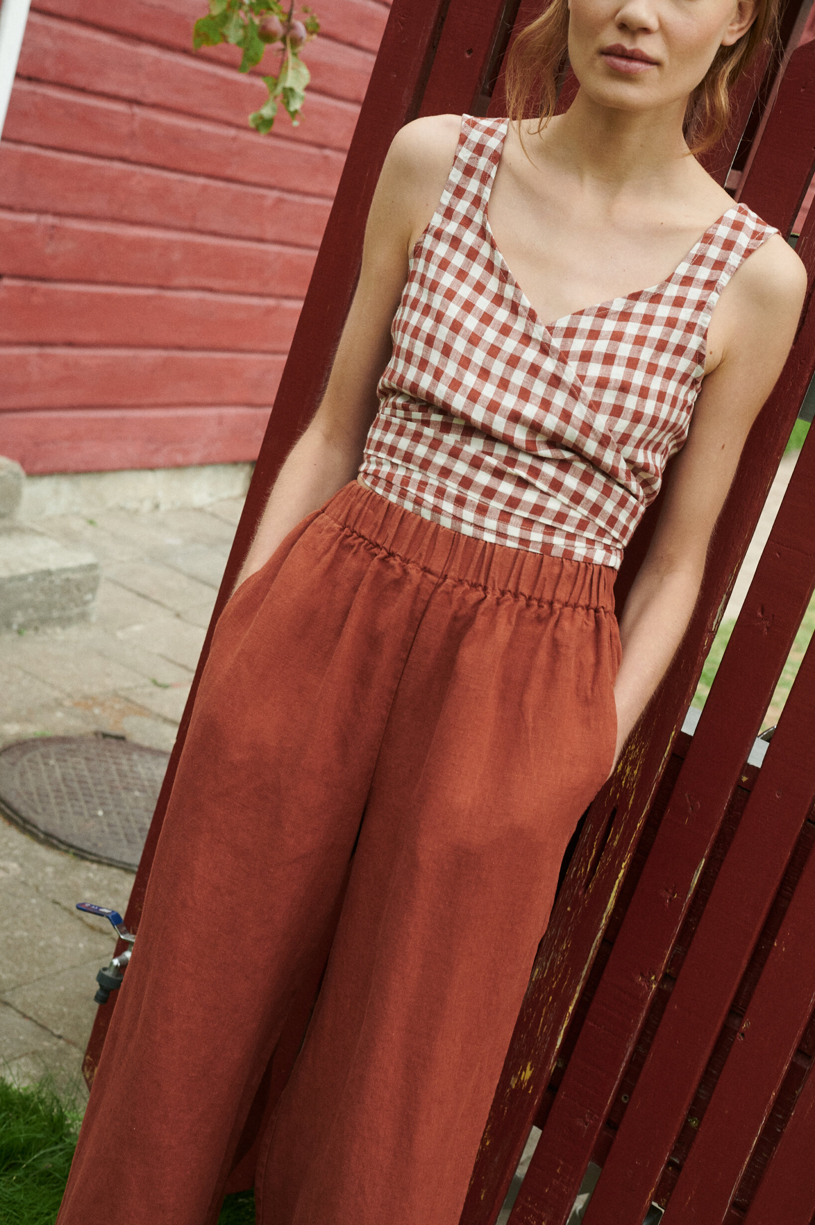 a close up shot of a model wearing a terrracotta gingham linen wrap top and wide leg trousers in terracotta linen