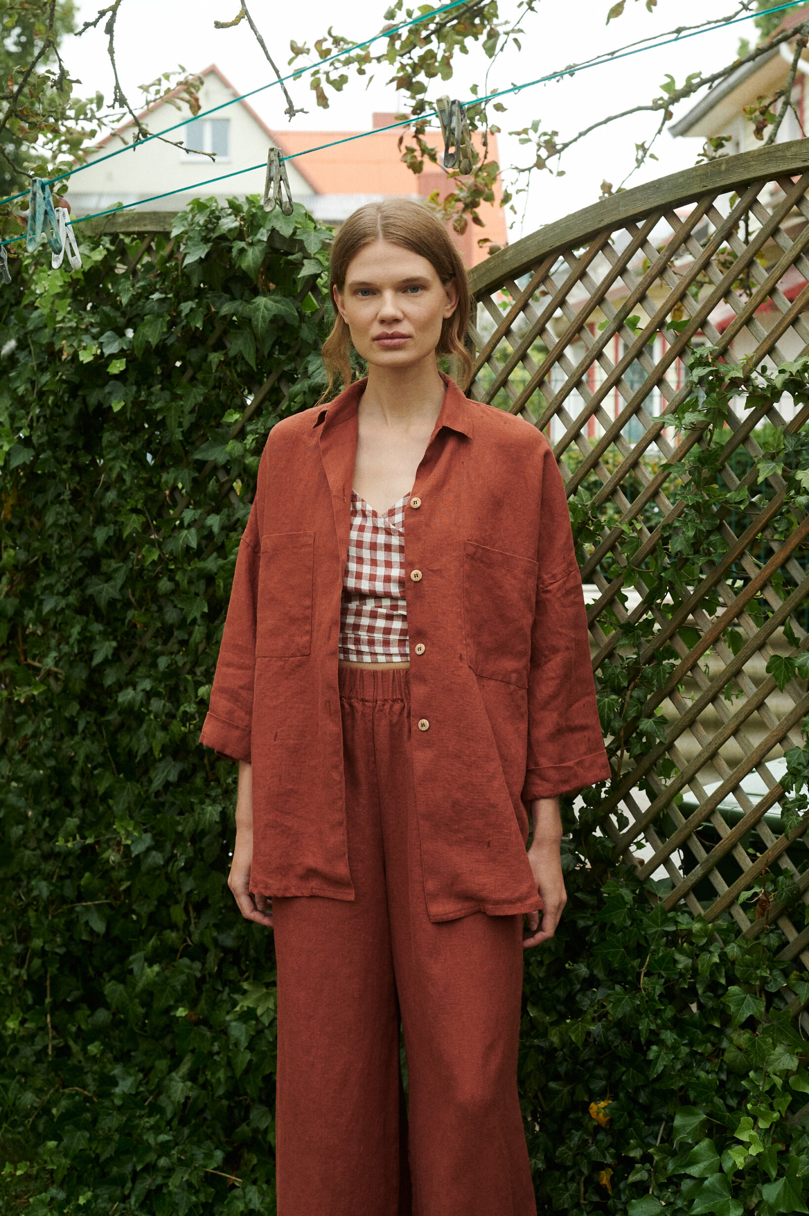 model in a garden wearing a terrracotta gingham linen wrap top and wide leg trousers and jacket in terracotta linen