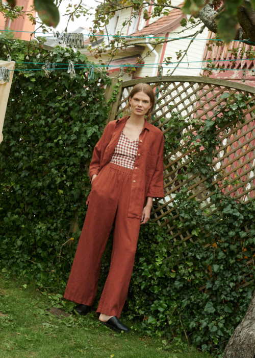model in a garden wearing a terrracotta gingham linen wrap top and wide leg trousers and shirt in terracotta linen