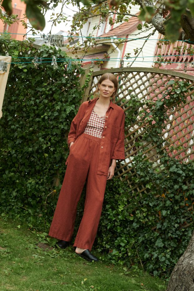 model in a garden wearing a terrracotta gingham linen wrap top and wide leg trousers and shirt in terracotta linen