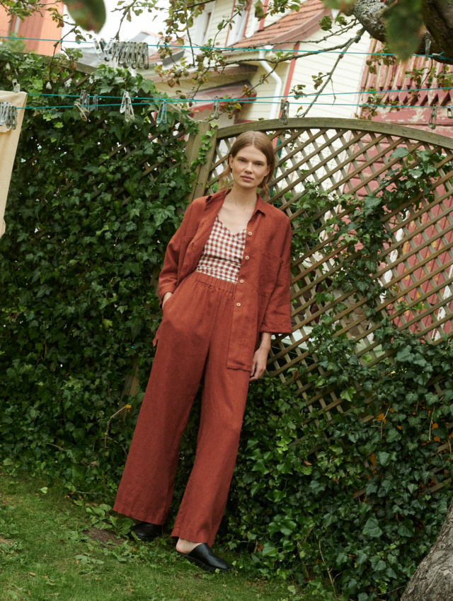 model in a garden wearing a terrracotta gingham linen wrap top and wide leg trousers and shirt in terracotta linen