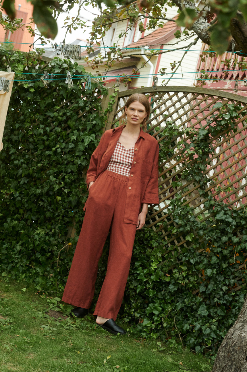 model in a garden wearing a terrracotta gingham linen wrap top and wide leg trousers and shirt in terracotta linen