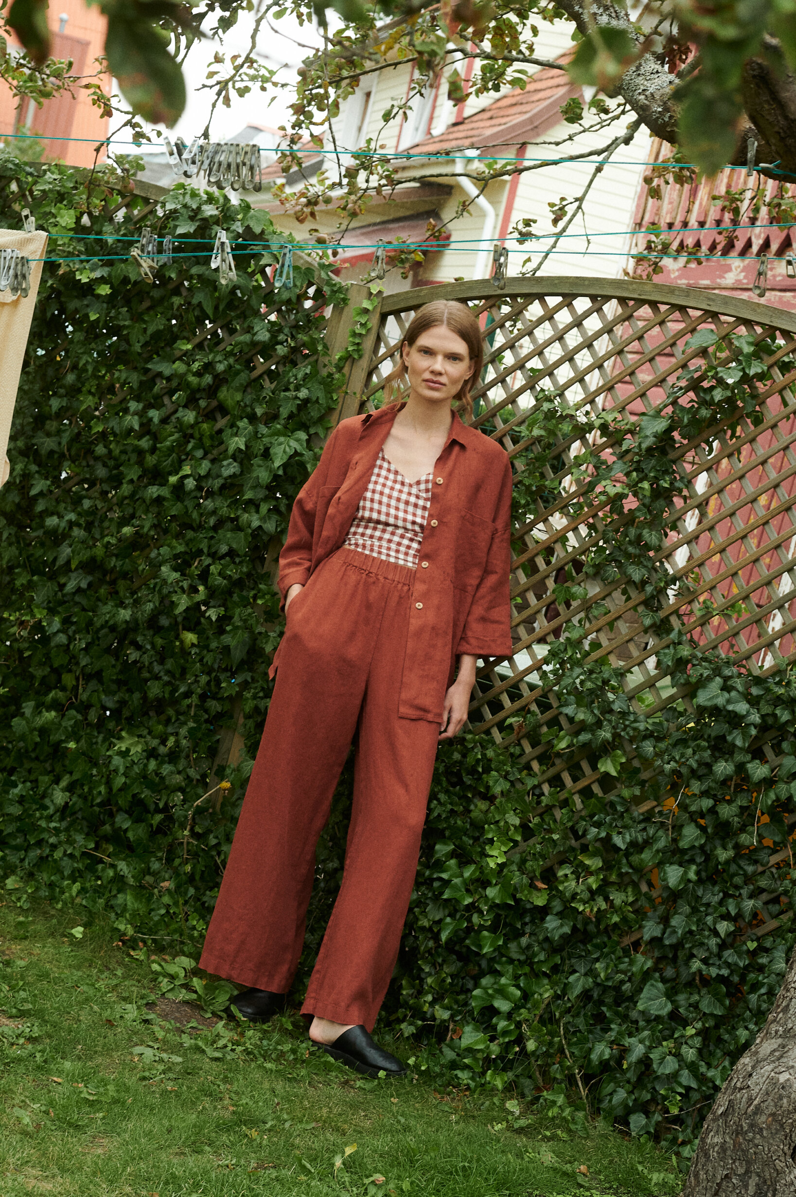 model in a garden wearing a terrracotta gingham linen wrap top and wide leg trousers and shirt in terracotta linen