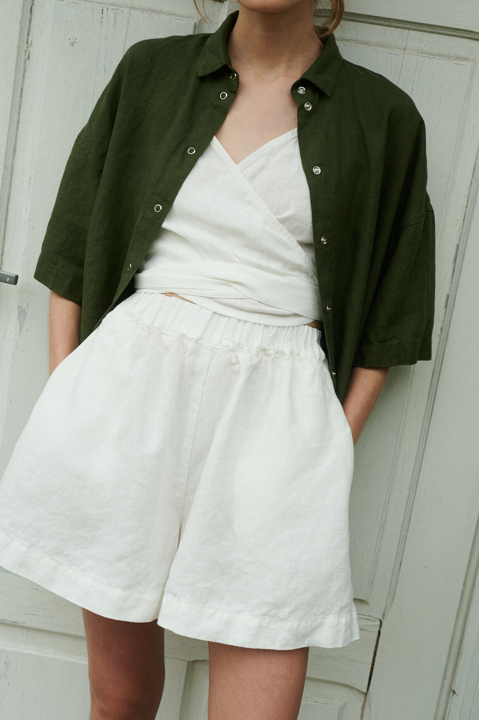 a close up shot of summer linen set in wide milky white shorts and v-neck wrap top, along with forest green shirt