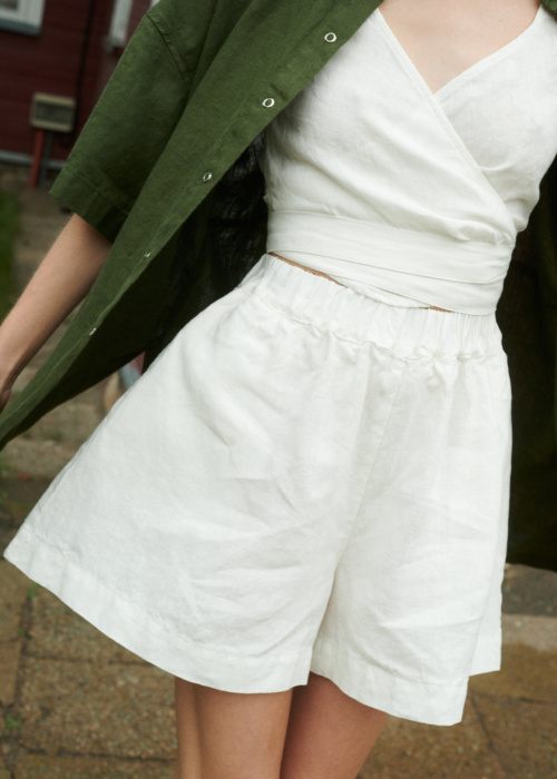 woman wearing natural linen wide summer shorts in milky white and v-neck wrap top along with forest green shirt