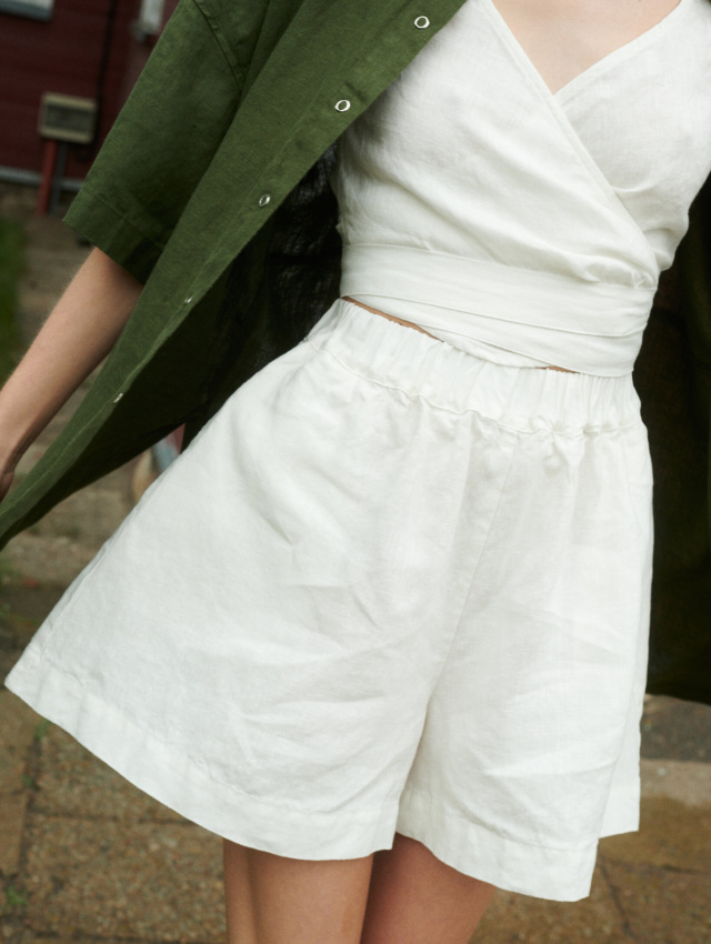 woman wearing natural linen wide summer shorts in milky white and v-neck wrap top along with forest green shirt