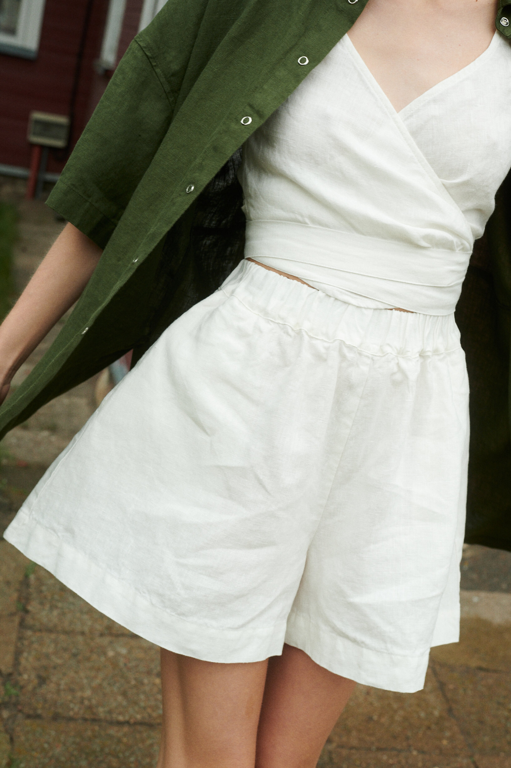 woman wearing natural linen wide summer shorts in milky white and v-neck wrap top along with forest green shirt