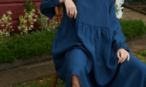 a close up shot of model sitting in a garden wearing oversized linen dress with full length sleeves in navy blue