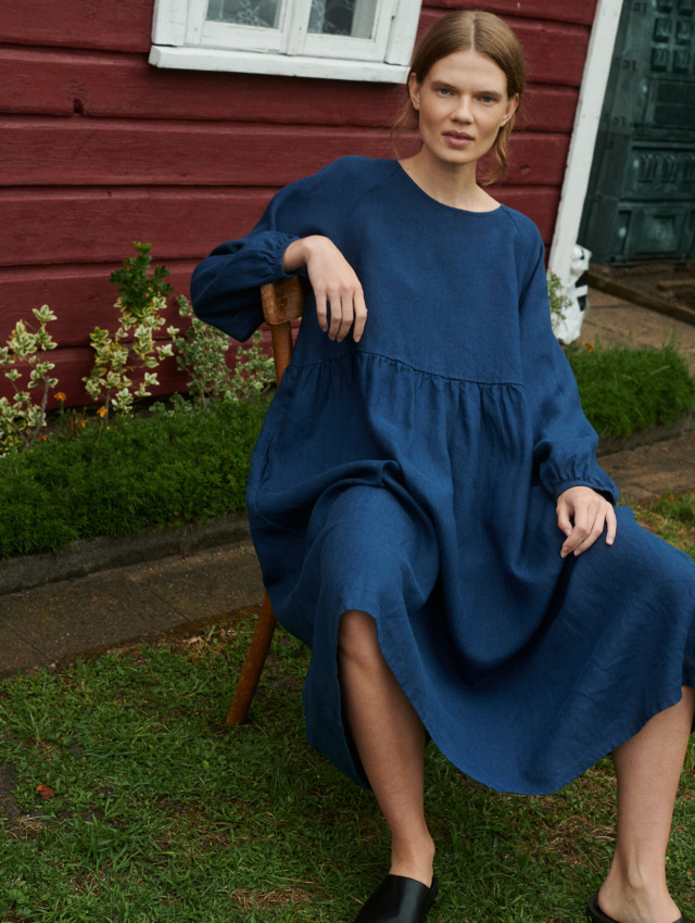 a close up shot of model sitting in a garden wearing oversized linen dress with full length sleeves in navy blue