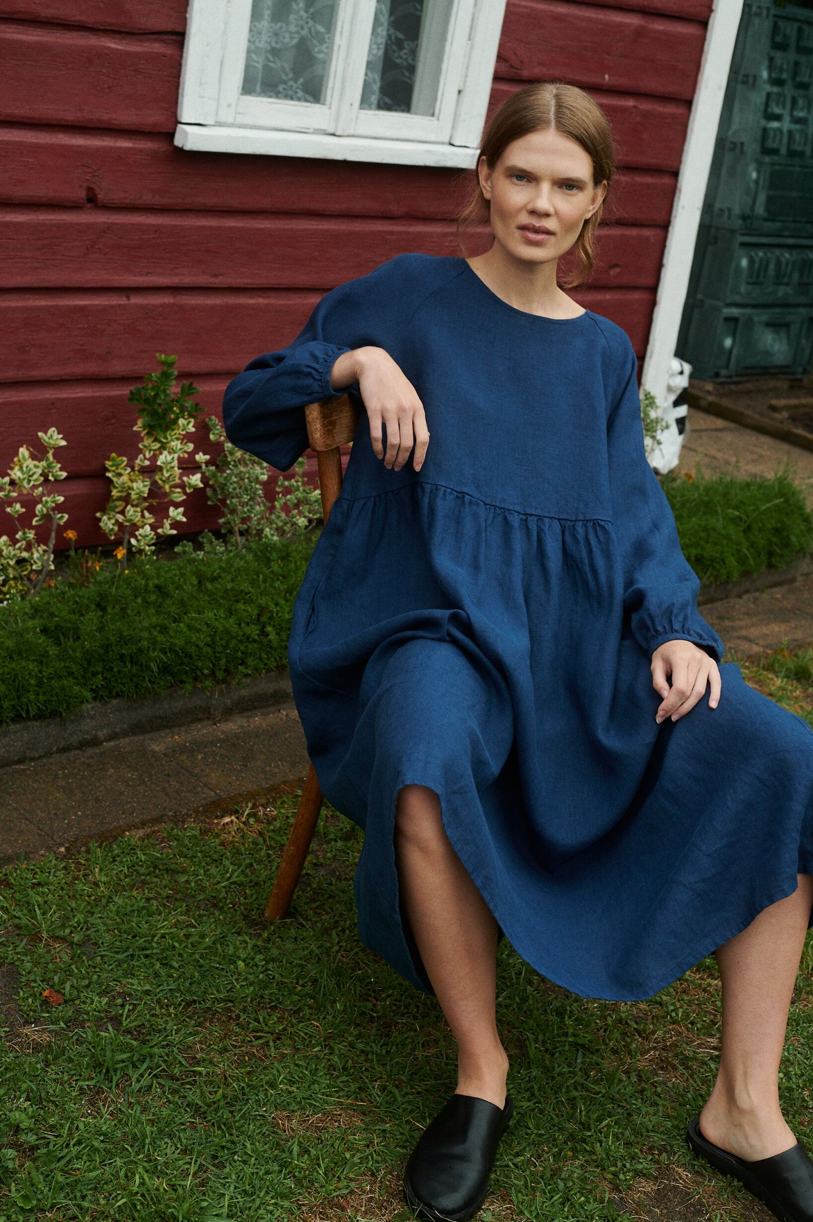 a close up shot of model sitting in a garden wearing oversized linen dress with full length sleeves in navy blue
