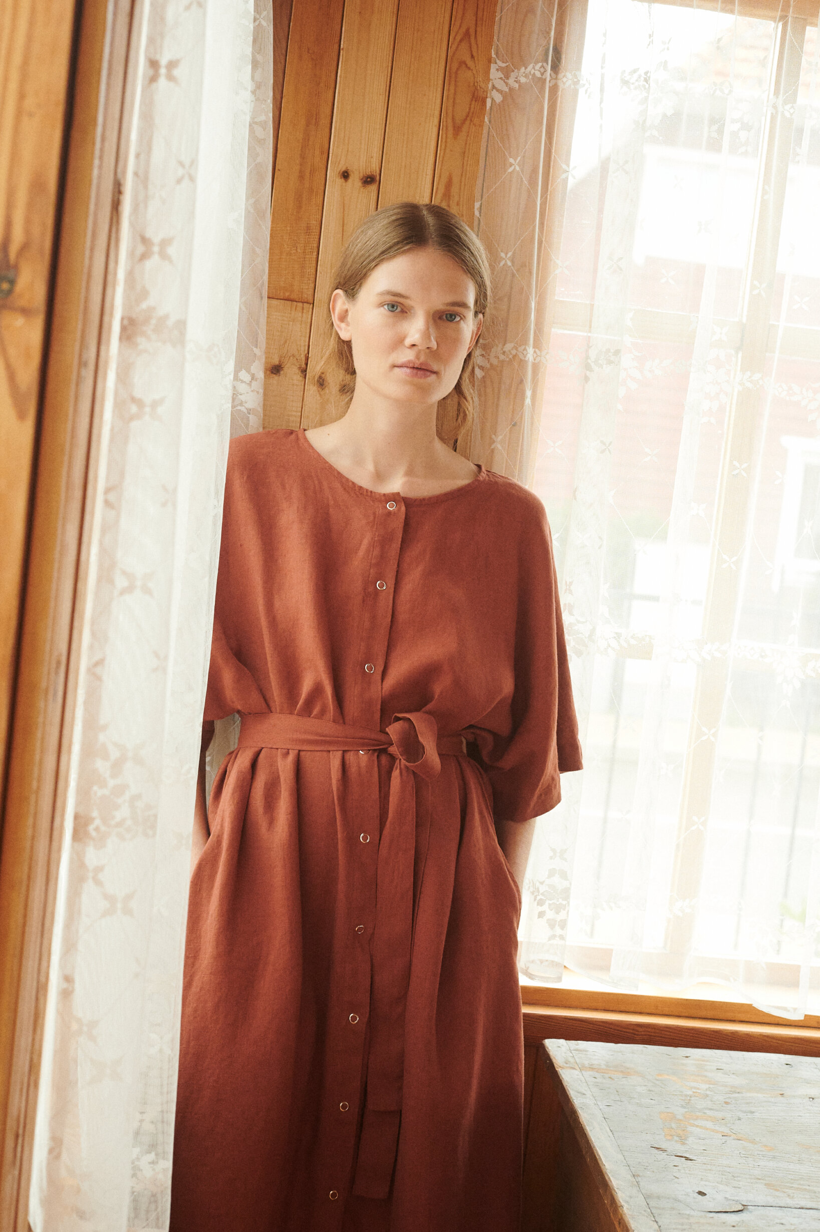 a close up short of a model wearing oversized linen dress in terracotta with snap openings and belt